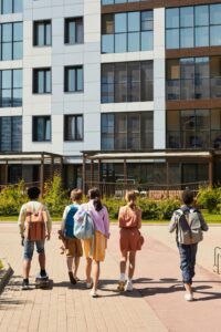 A group of teenagers walking towards a modern school building on a sunny day.